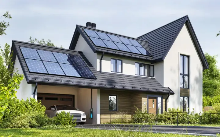 Nowoczesny dom z panelami fotowoltaicznymi na dachu. Obok stoi biały samochód z ładowarką. To właśnie oze co to – energia odnawialna w praktyce.